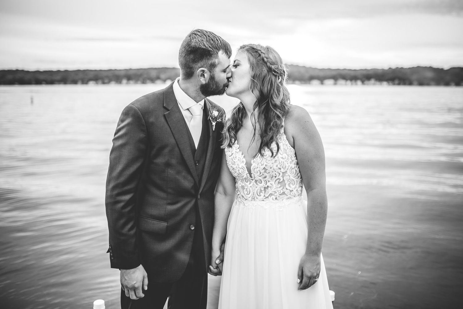 Newlyweds embrace on a wooden dock during a lakeside sunset celebration.