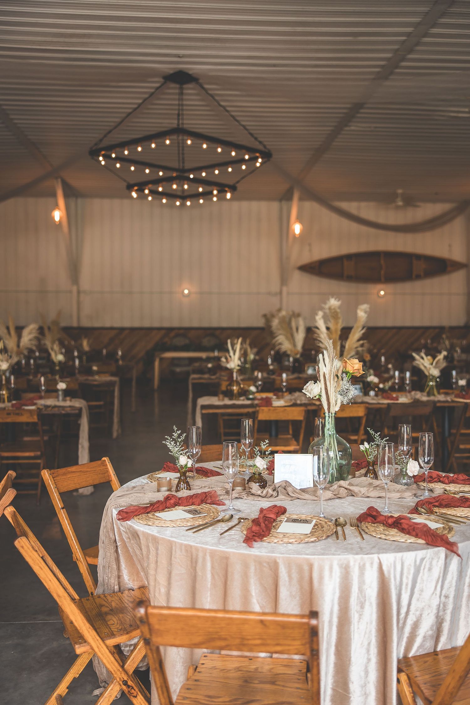 Elegant wedding reception tables set with white linens, floral centerpieces and wooden chairs under string lights.