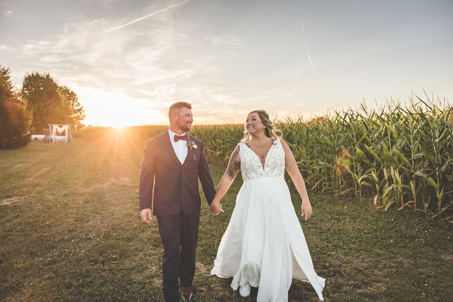 Wedding couple walks hand in hand through field during golden hour photography session.