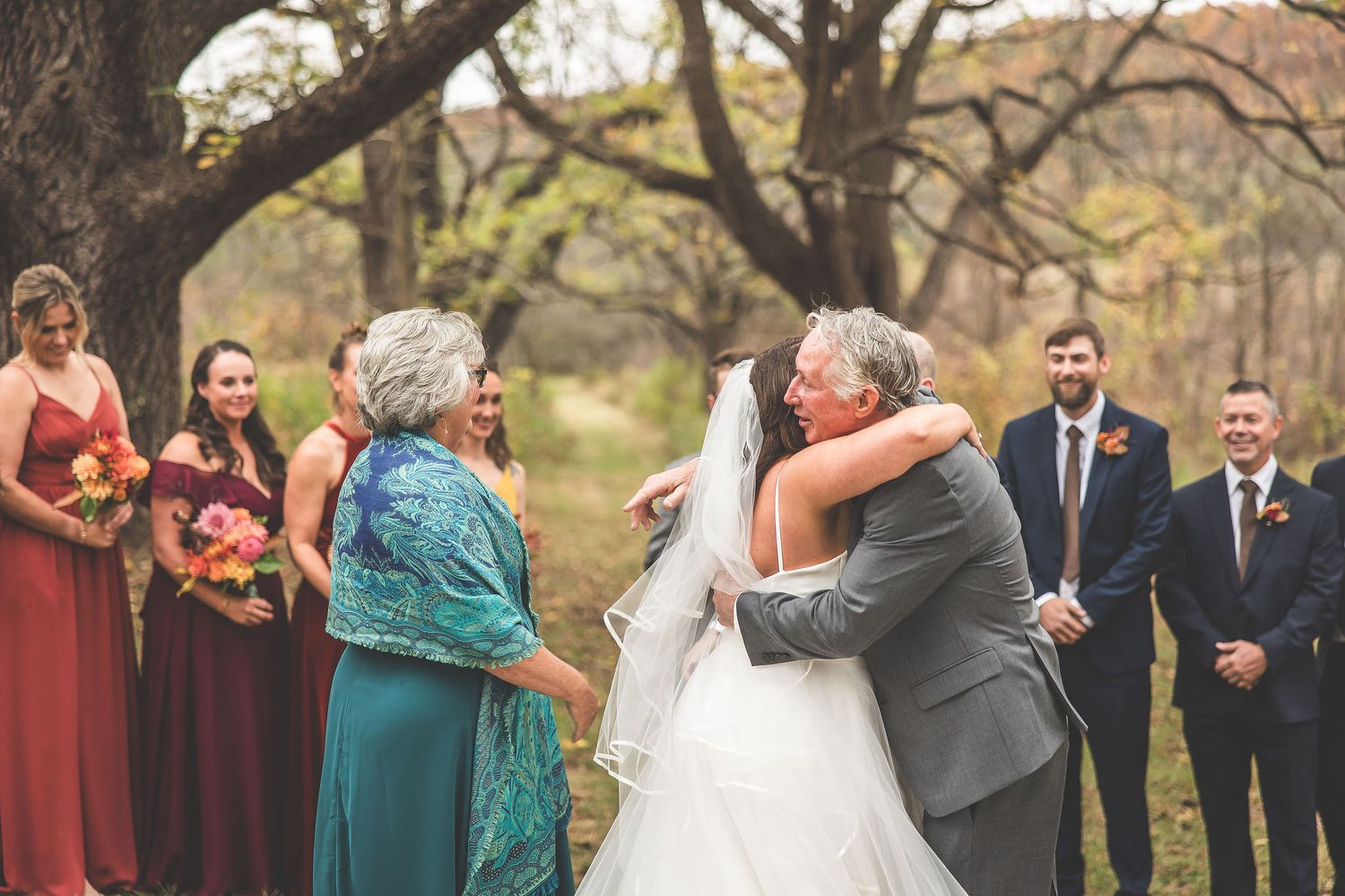 Wedding ceremony moment with bridesmaids in burgundy dresses watching an emotional embrace.