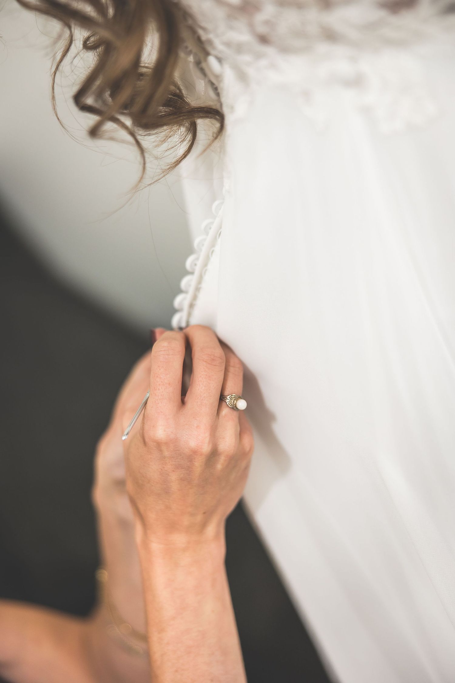 Close-up of hands buttoning delicate details on white wedding gown.