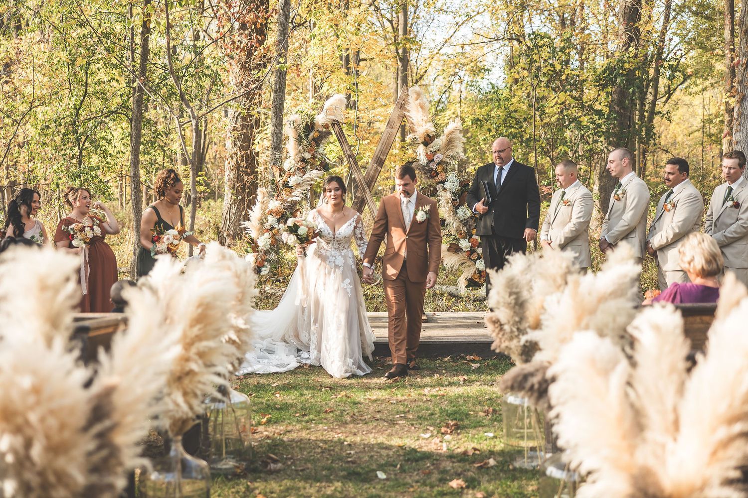 Outdoor fall wedding ceremony setup with rustic wooden arch decorated with pampas grass and autumn florals.