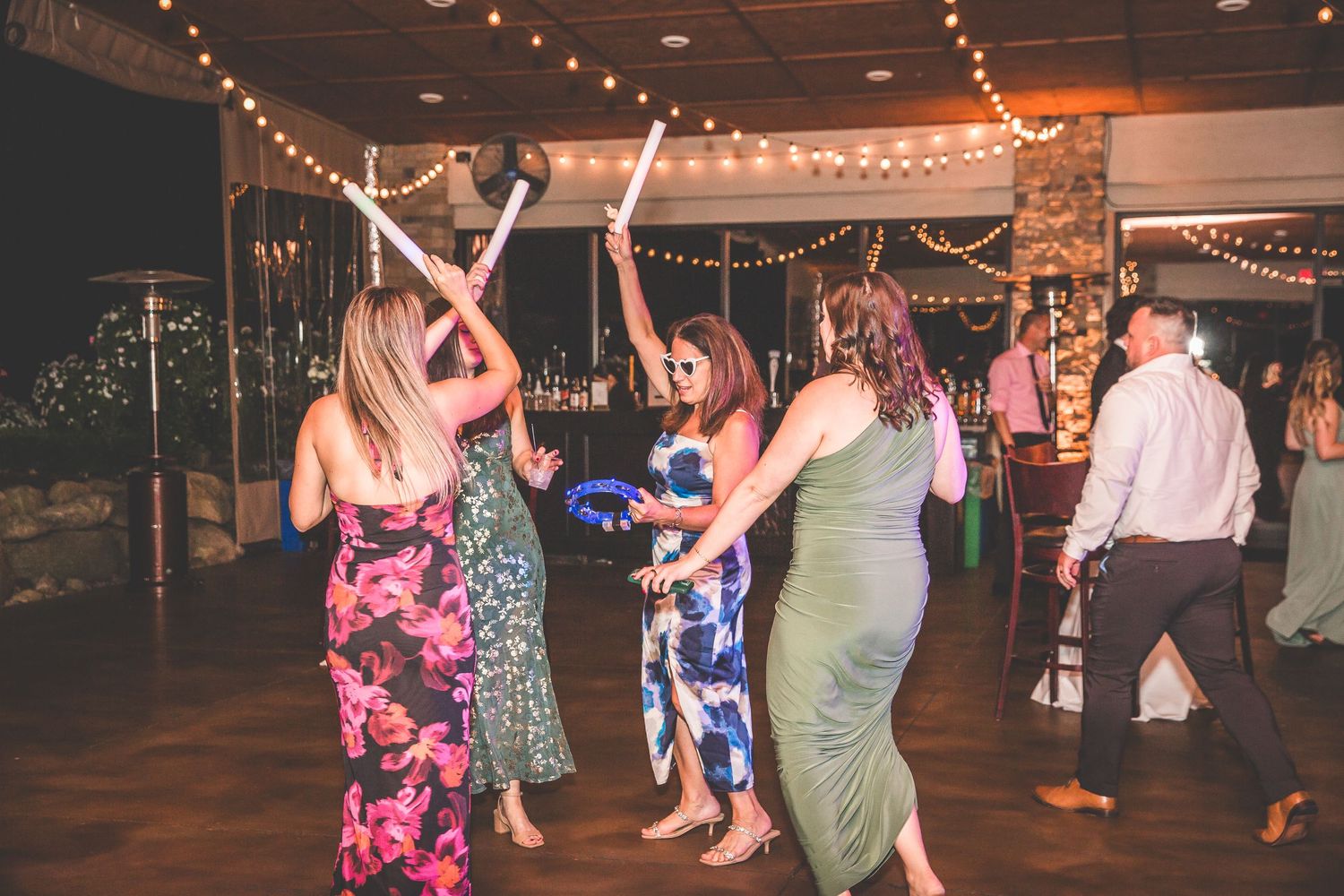 Wedding guests dancing under string lights at indoor reception venue.