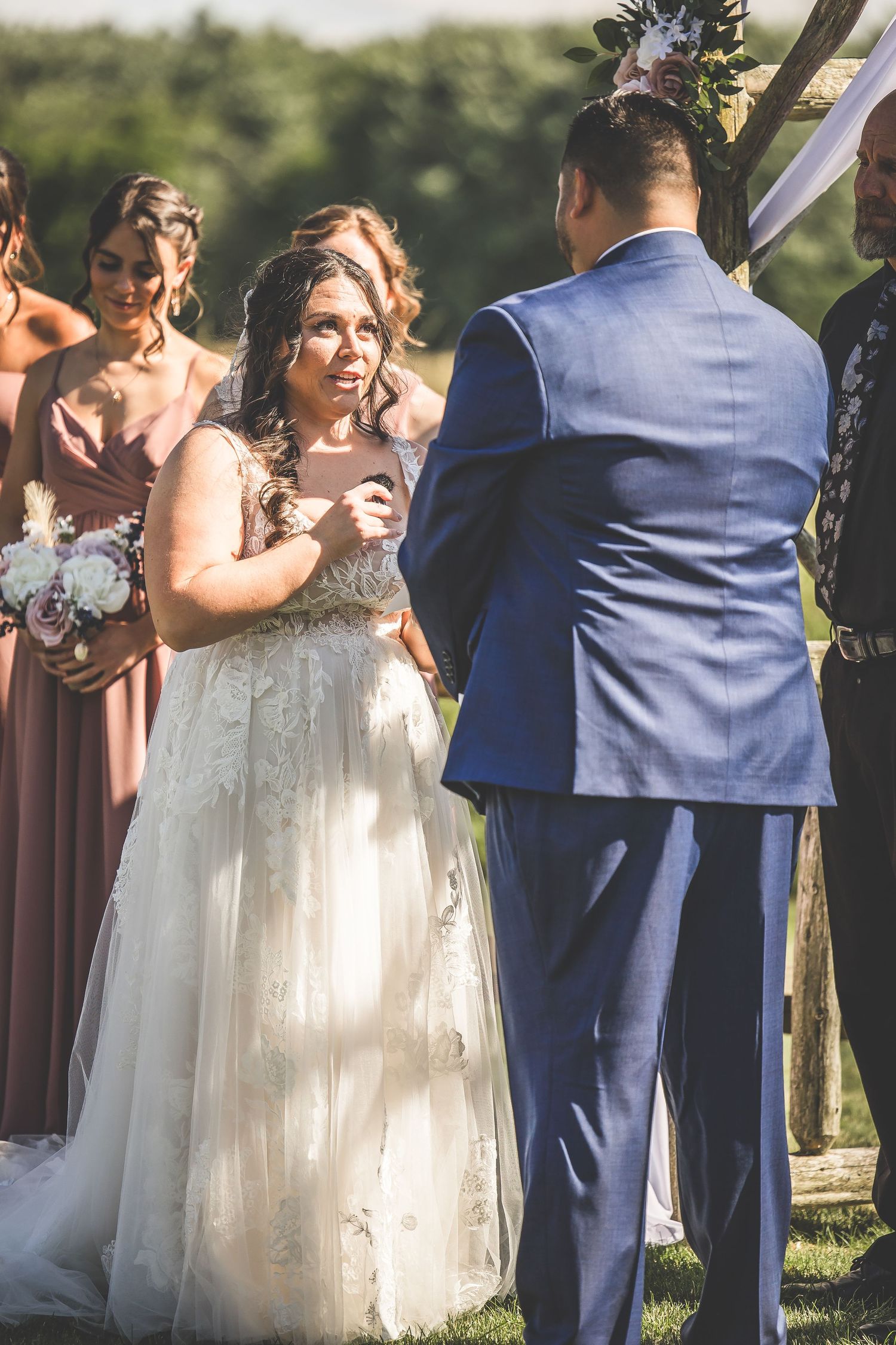 Joyful outdoor wedding ceremony with bridal party in navy suits and flowing white gowns.