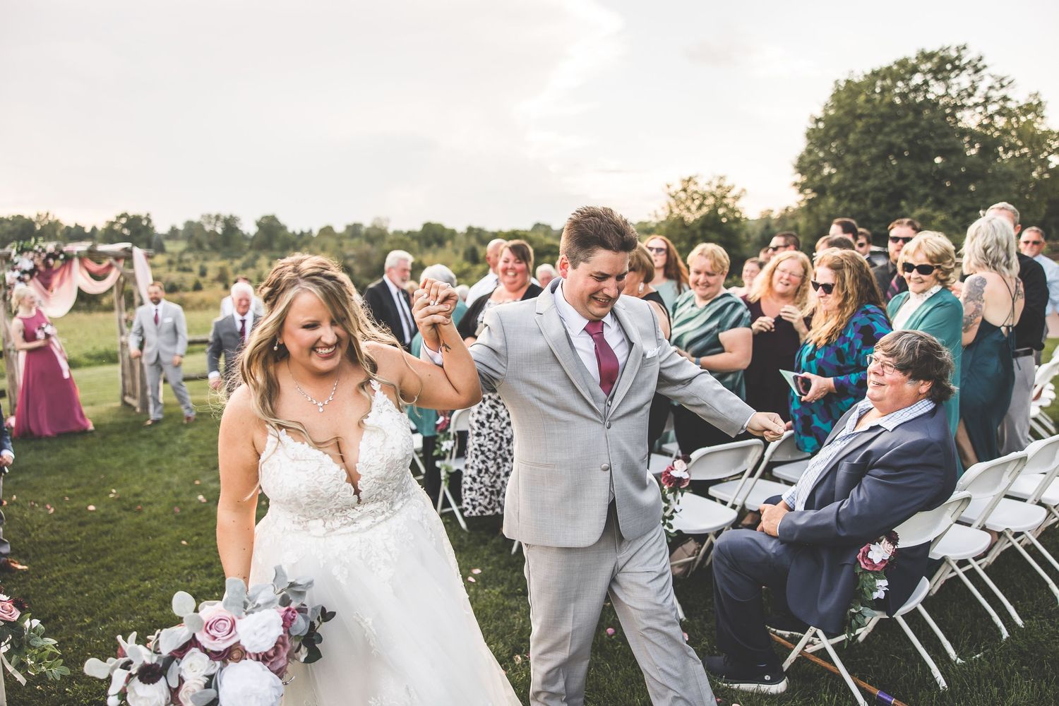Outdoor wedding ceremony with guests seated in rows of white chairs against a natural landscape backdrop.