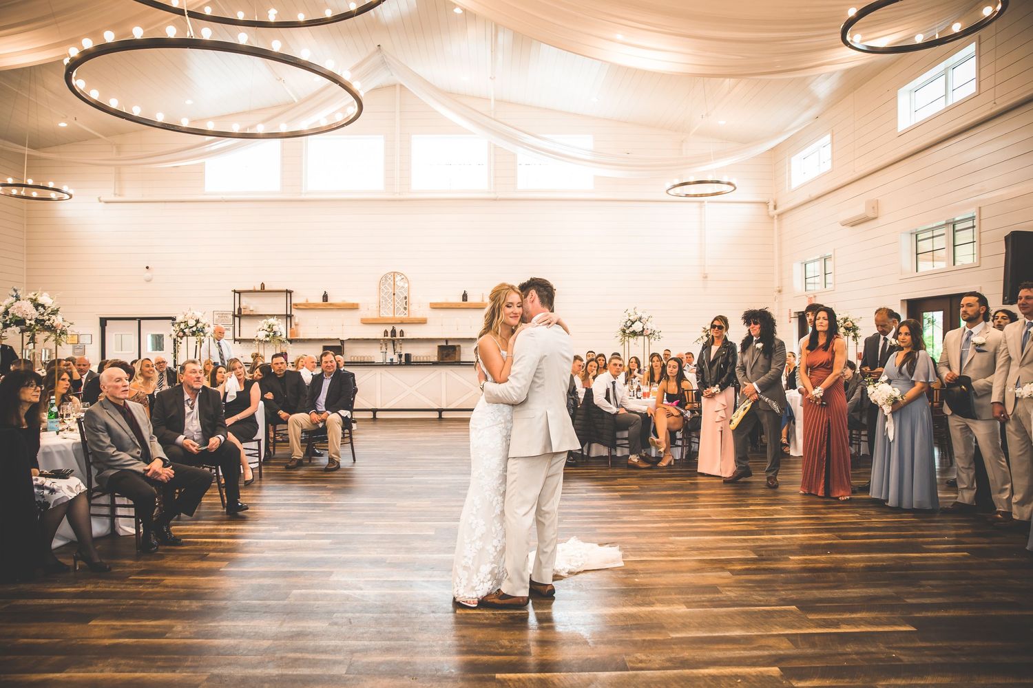 Wedding reception venue with circular chandeliers and white walls filled with celebrating guests.