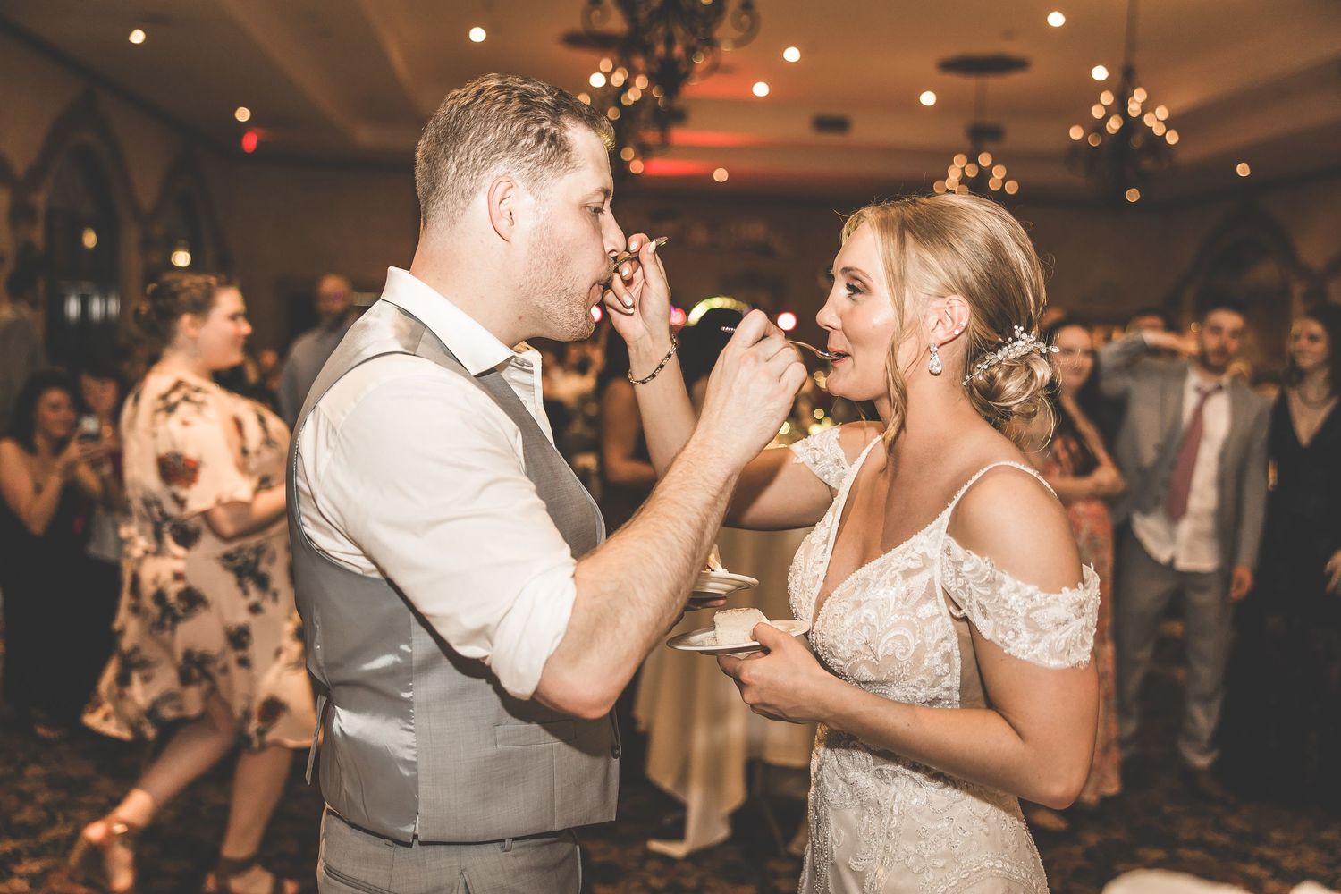 Wedding guests dancing and celebrating at an indoor reception with warm lighting and festive atmosphere.