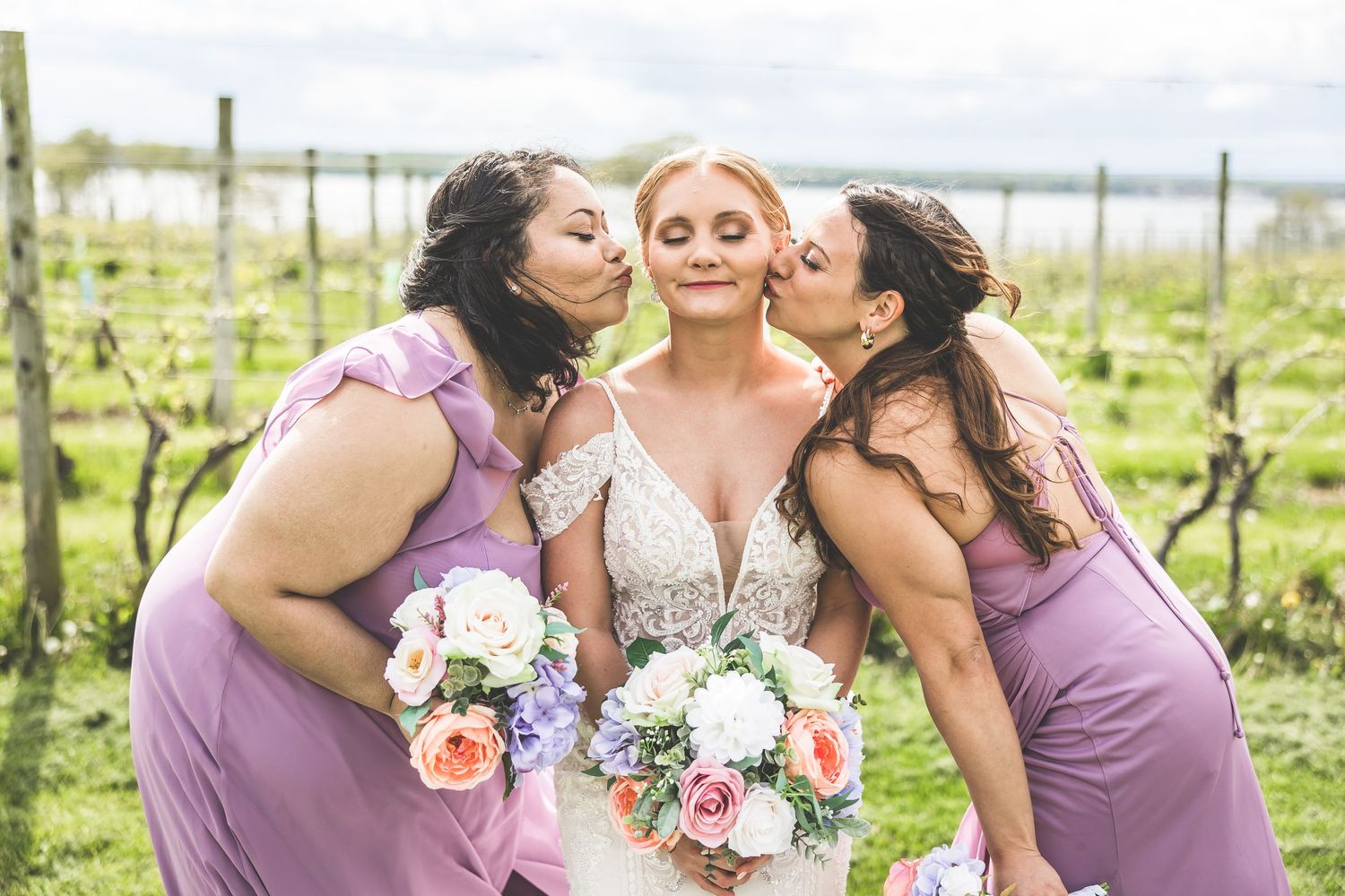 Bridesmaids in purple dresses sharing intimate moments with the bride in a vineyard setting.