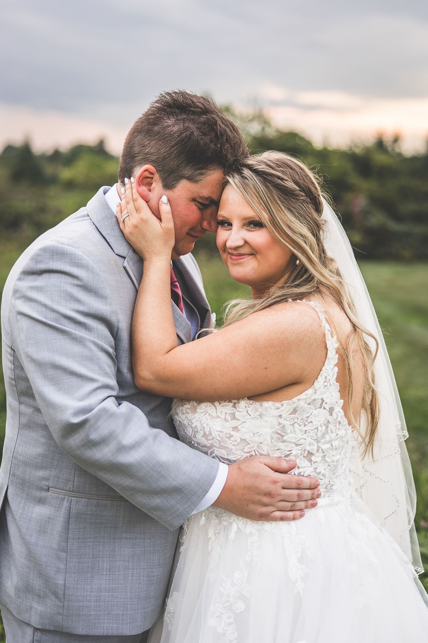 Intimate wedding portrait in field at sunset with couple sharing tender moment.