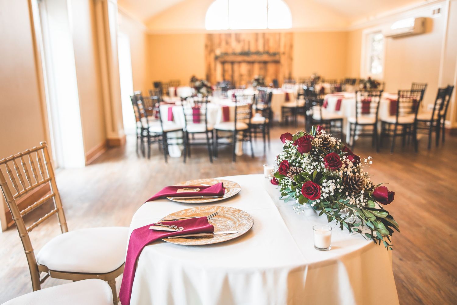 Wedding reception venue with elegant table settings featuring burgundy accents and floral centerpieces.