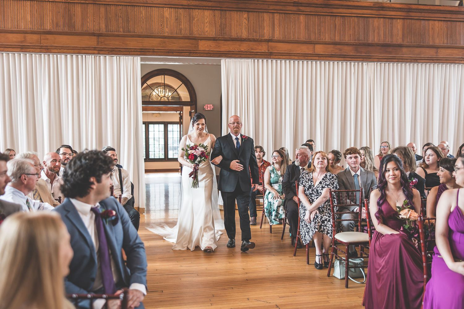 Wide view of wedding ceremony in elegant hall with guests seated on both sides.
