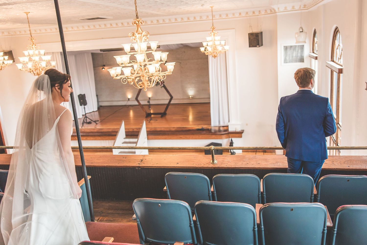 Wedding venue interior featuring blue chairs and crystal chandeliers in warm lighting.