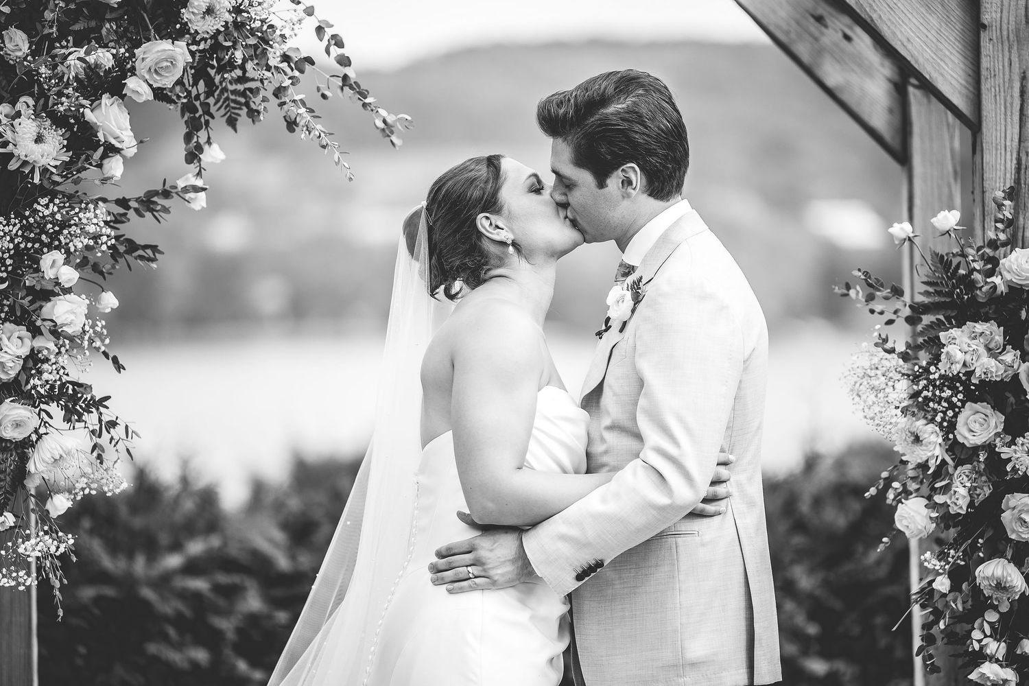 Black and white portrait of couple sharing romantic moment under floral arch.