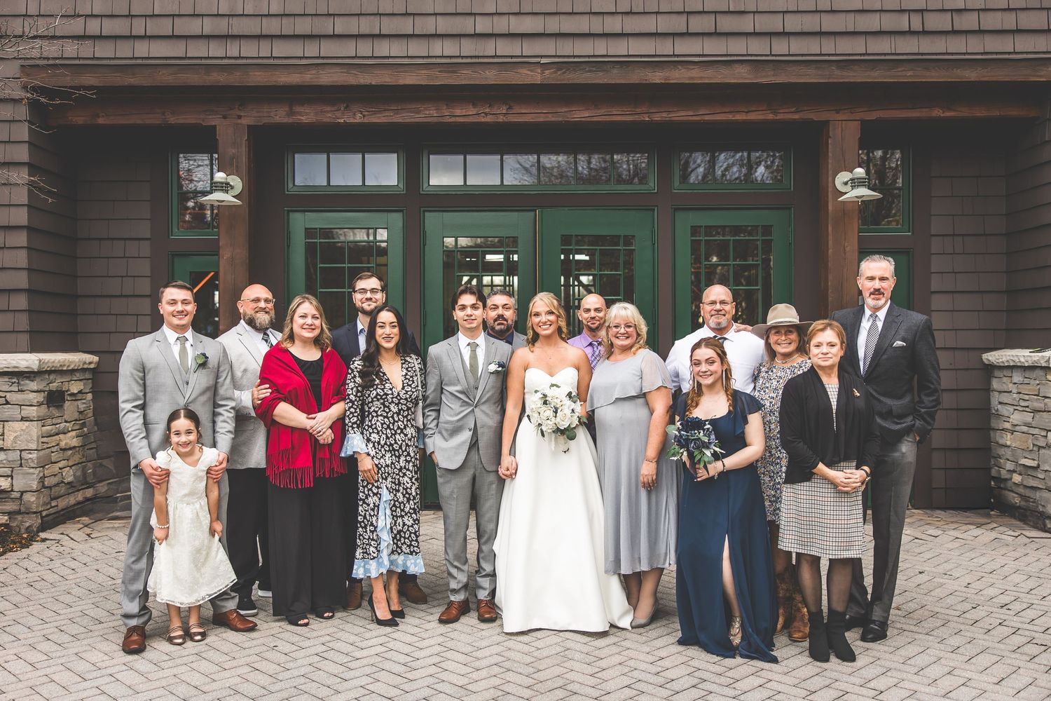 Large group photo of wedding guests gathered outside a brick and stone building.