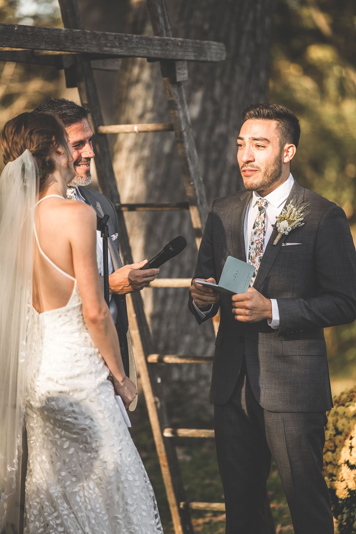 Wedding officiant reading from book during outdoor ceremony under wooden arch.
