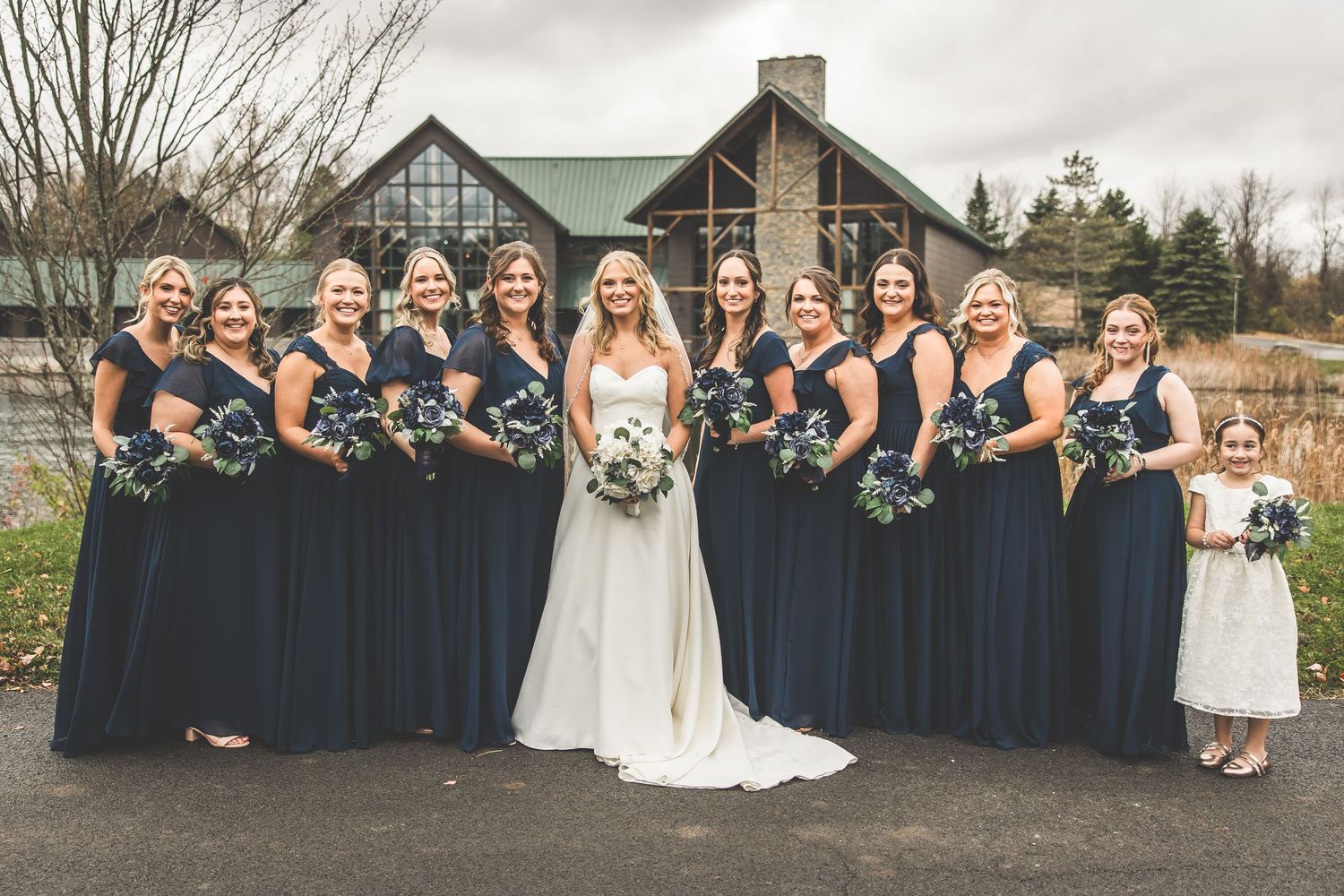 Wedding party in navy blue and white attire poses for group photo outdoors.