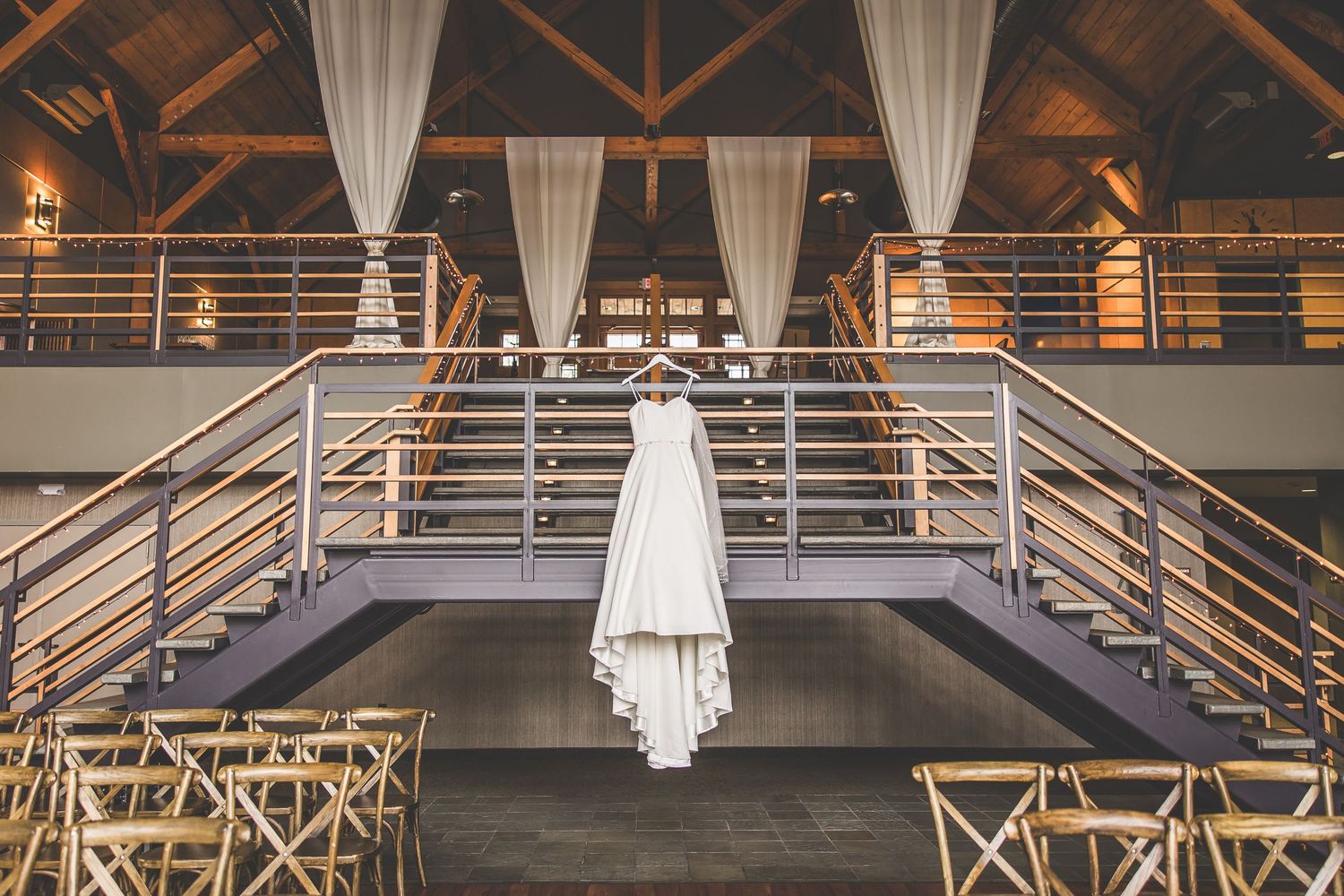 White wedding dress hangs elegantly from metal railings in a modern venue with draped fabric.