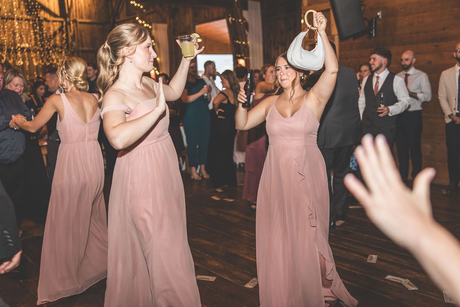 Bridesmaids in pink dresses dancing and celebrating at wedding reception.