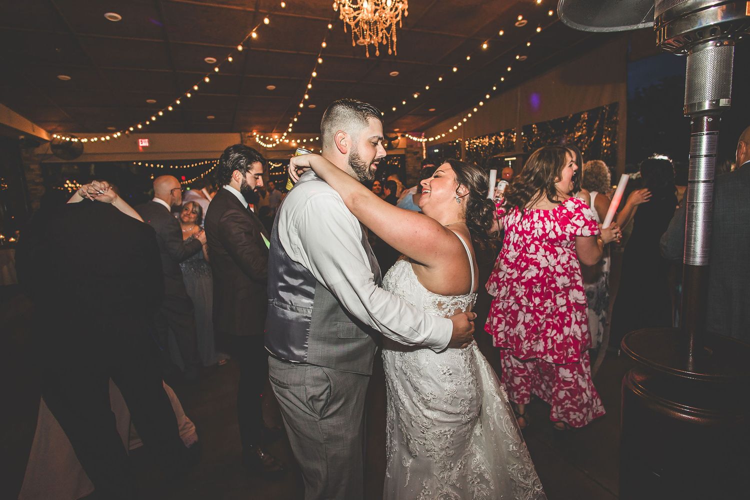 Couple sharing a romantic dance moment at their wedding reception under string lights.