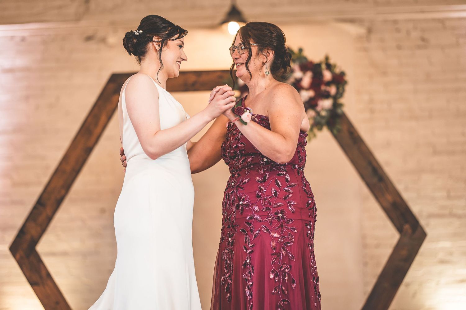 Two people sharing a joyful moment during a wedding reception under decorative lighting.