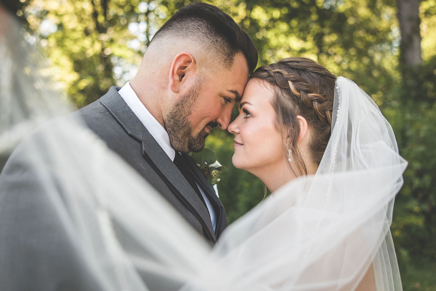 Intimate wedding portrait captured under flowing veil in outdoor setting.