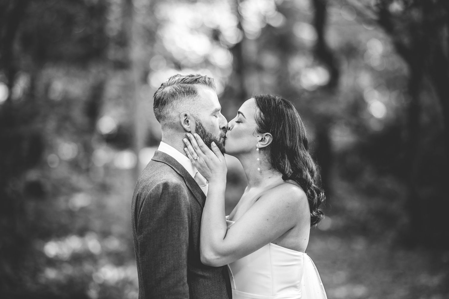 Black and white portrait of a tender wedding moment captured in a forest setting.