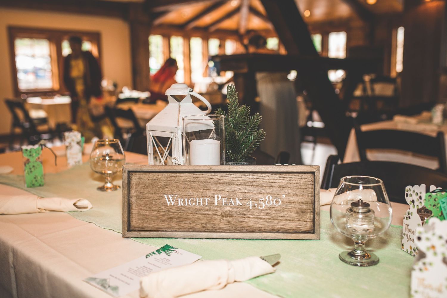 Rustic wedding reception tables decorated with wooden centerpieces and greenery in warm lighting.