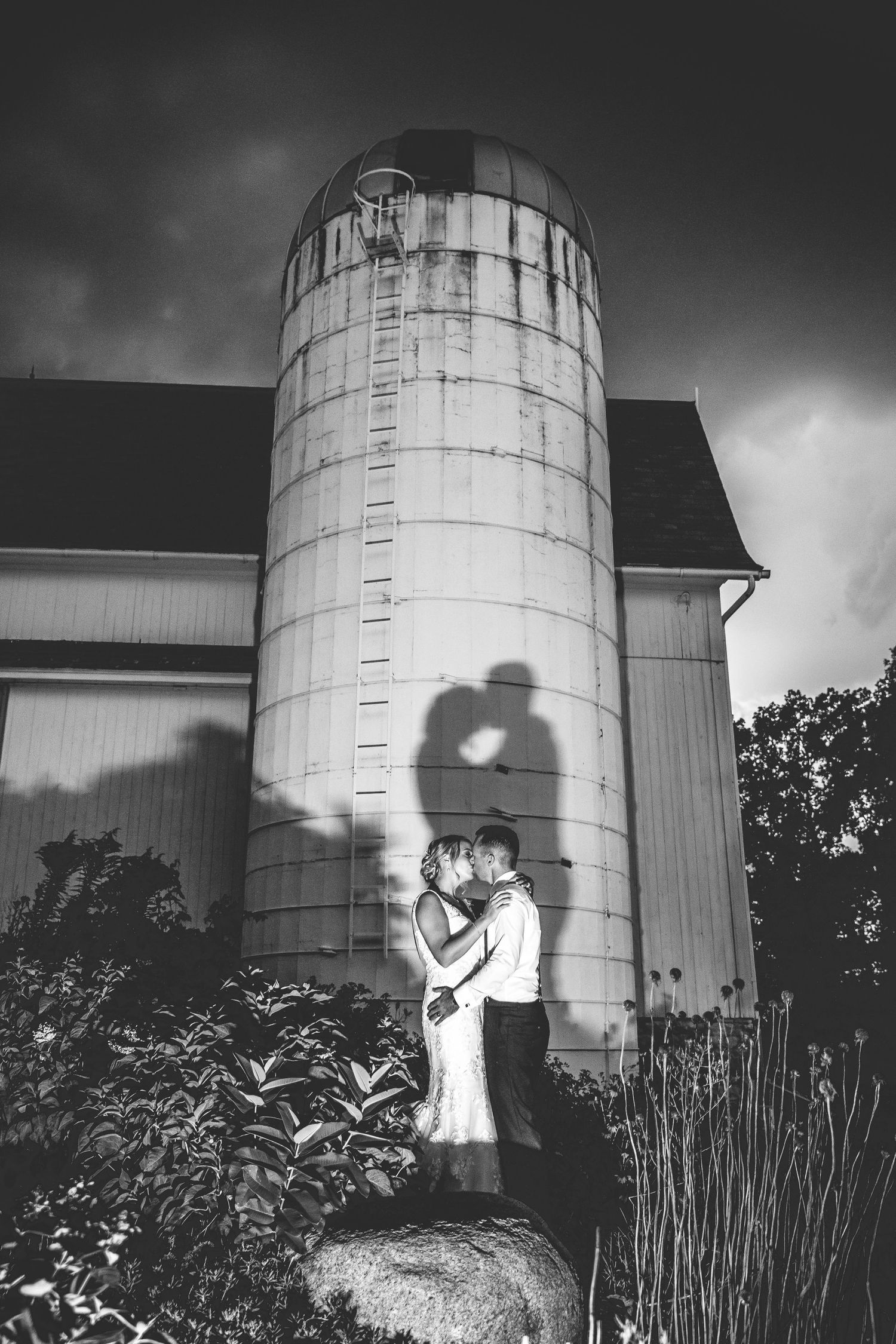 A dramatic black and white silhouette of a couple against a large farm silo.