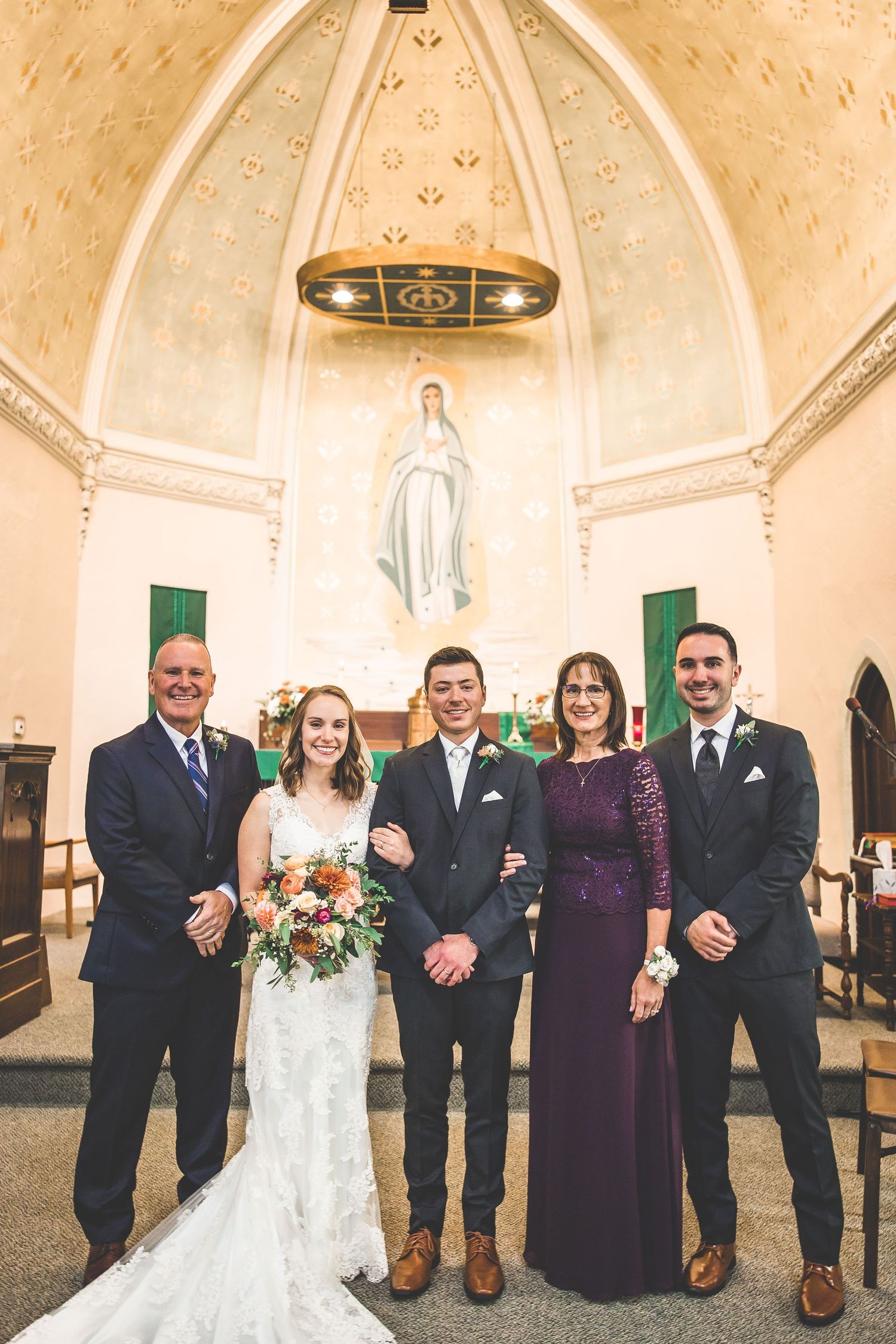 Wedding party poses for formal photos inside a church with vaulted ceiling and religious artwork.
