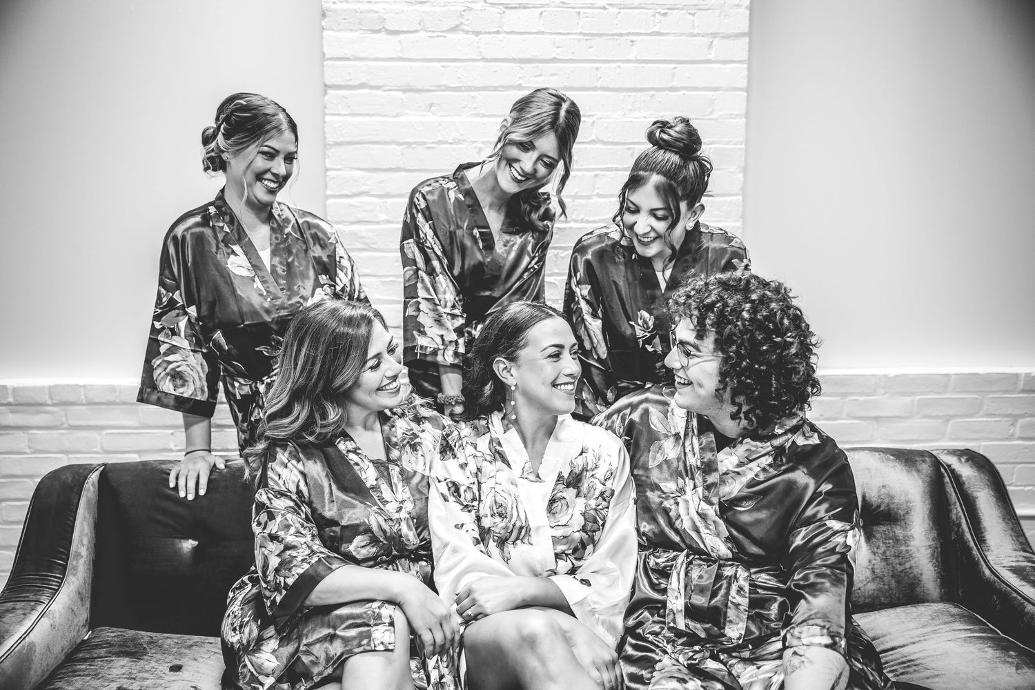 Black and white photo of wedding party in matching robes sharing joyful moment.