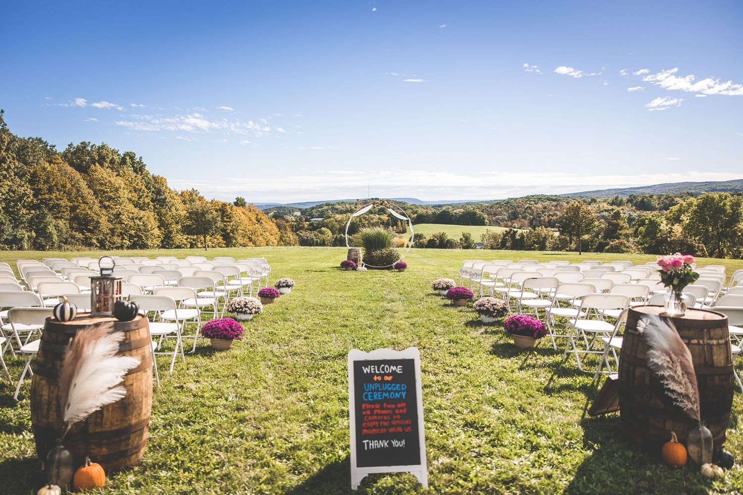 Outdoor wedding ceremony setup with rows of chairs and fall foliage in background.