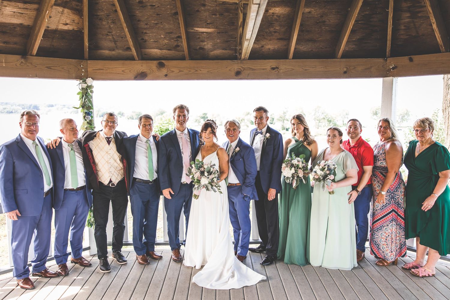Full wedding party poses in formation on rustic covered deck with wooden beams.