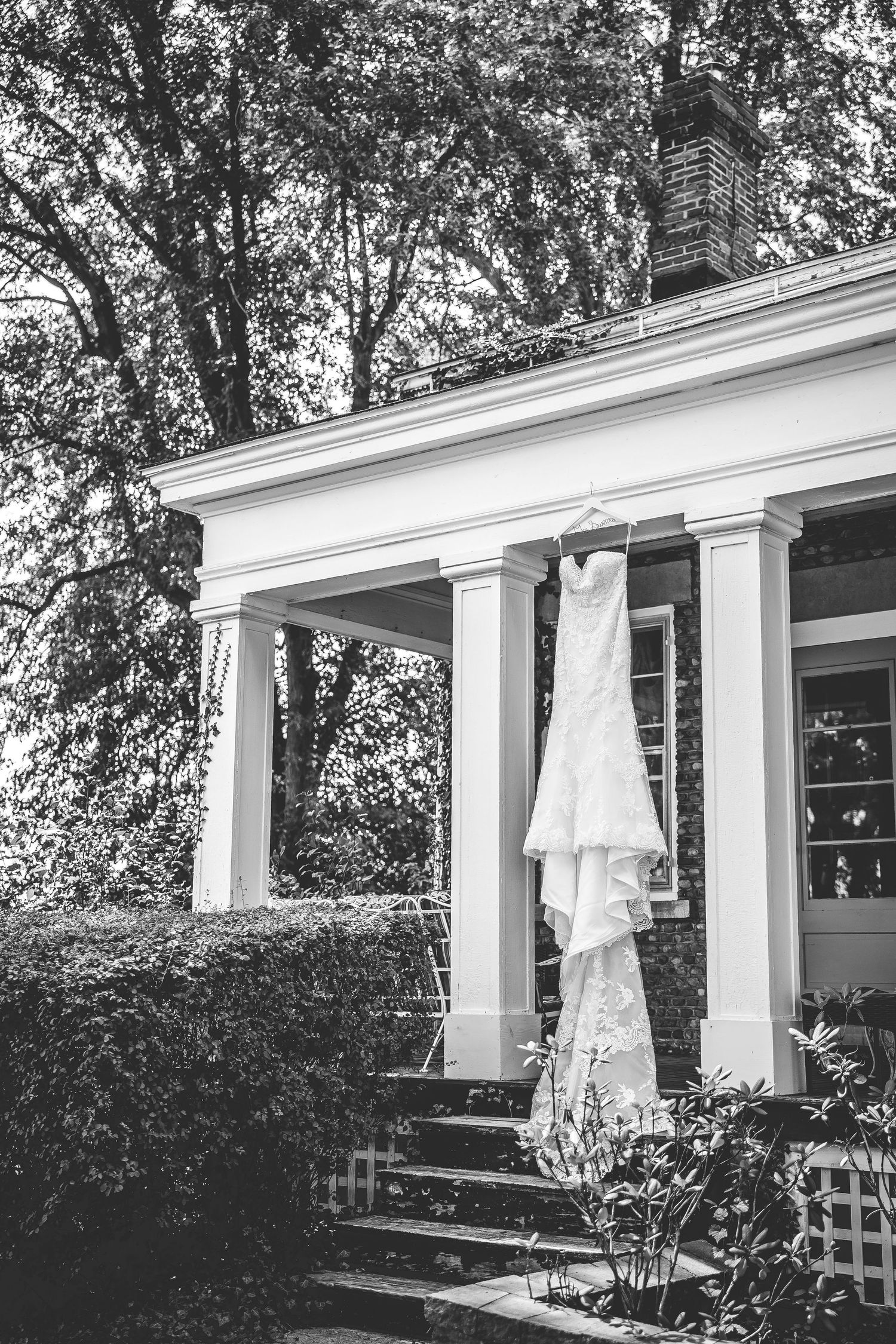 Black and white photo of a wedding dress hanging on a white columned porch.