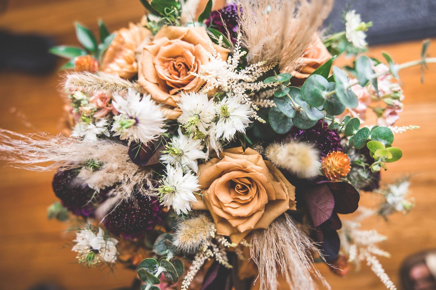 Elegant wedding bouquet featuring peach roses and mixed flowers on wooden surface.