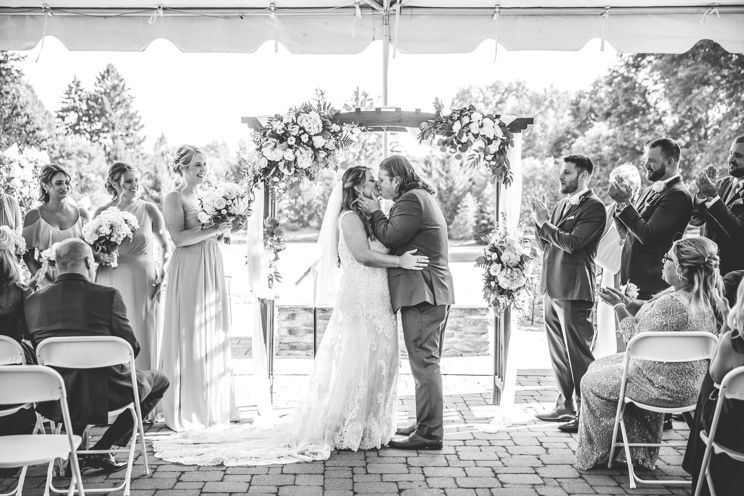 Wedding reception setup under a white tent with elegant table settings and floral arrangements.