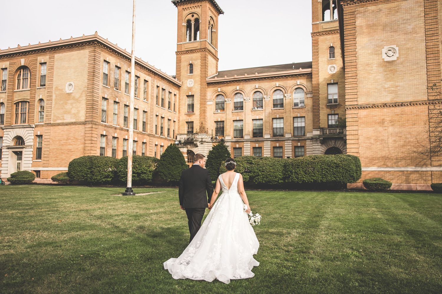 Historic brick building with towers and manicured lawn creates stunning wedding backdrop.