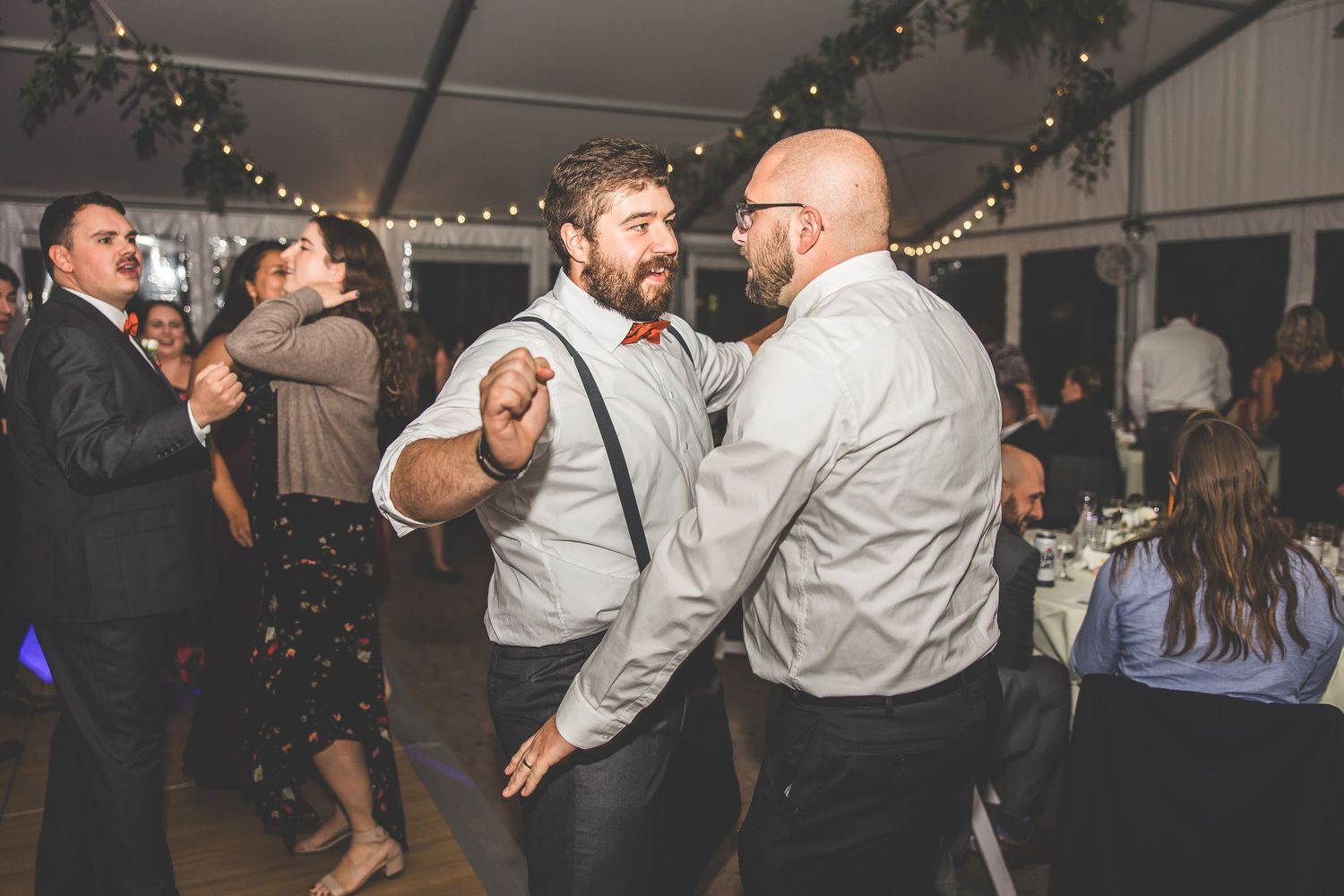 Wedding guests dance and celebrate on a dimly lit dance floor with string lights overhead.