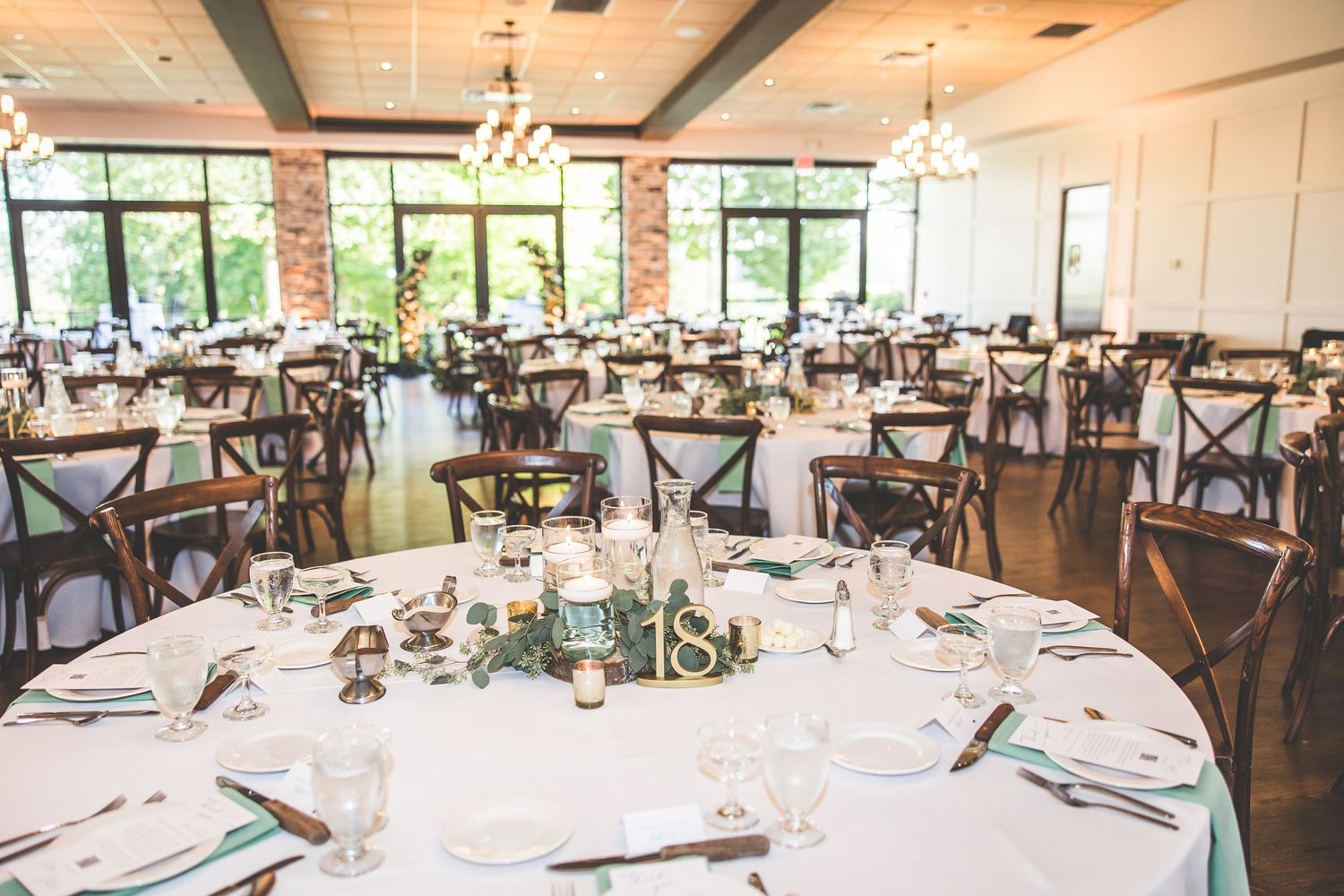 Wedding reception venue with round tables set for dining under exposed ceiling beams.