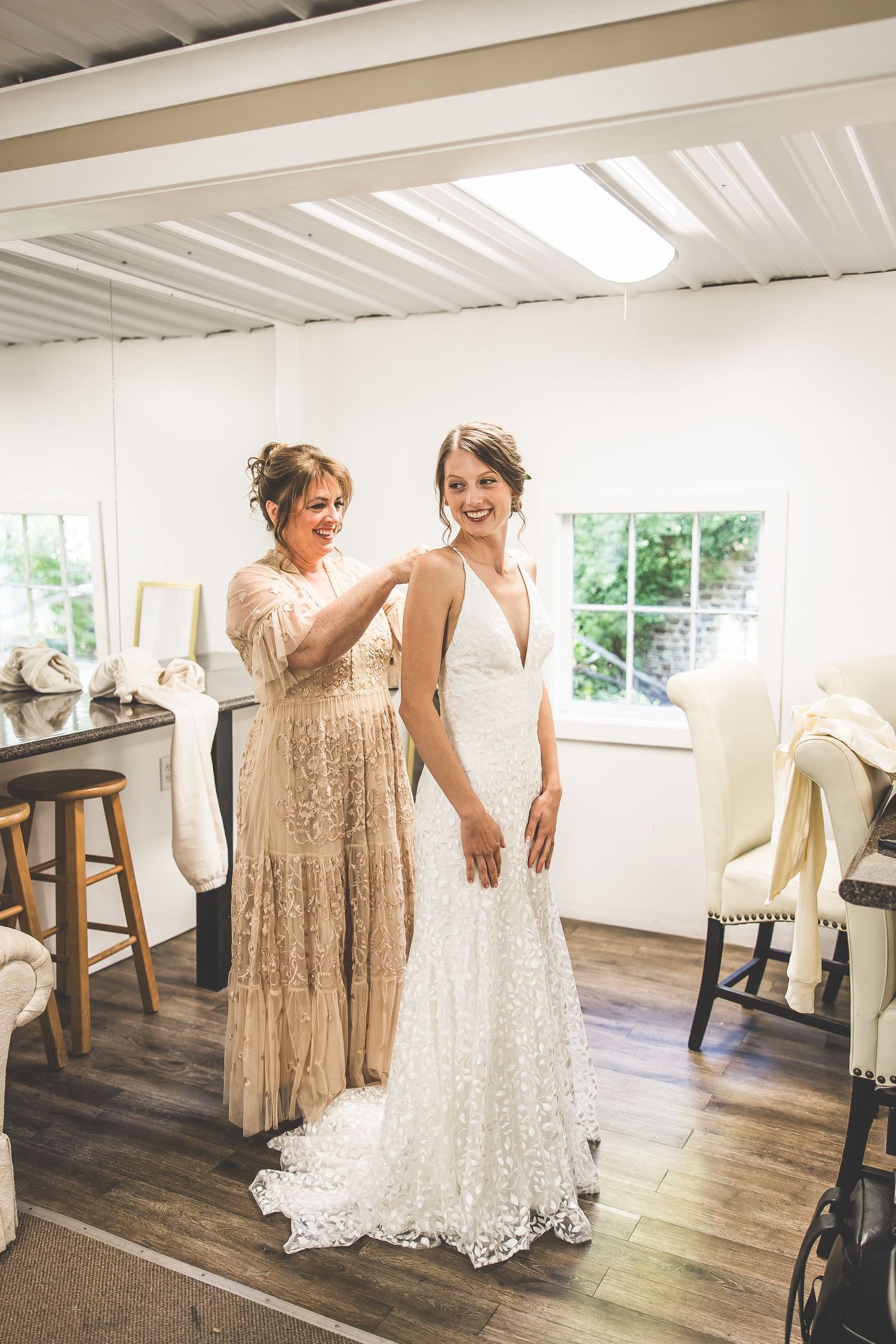 Two people in formal dresses dance and laugh together in a bright indoor space.