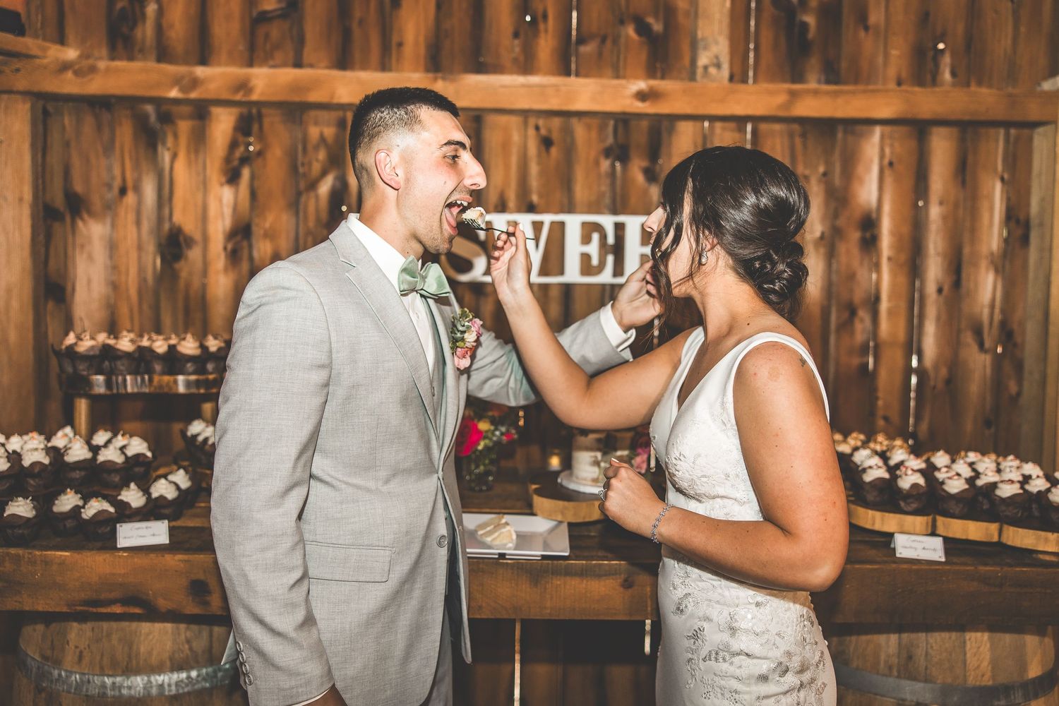 A playful cake-feeding moment between the couple at their rustic barn wedding reception.