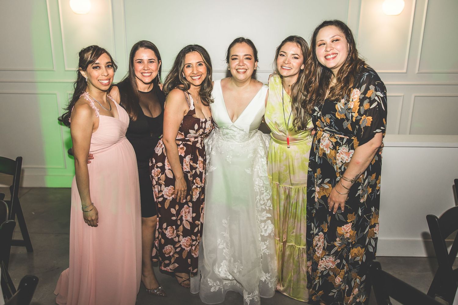 Wedding party guests in floral dresses and formal attire pose together at an elegant indoor venue.