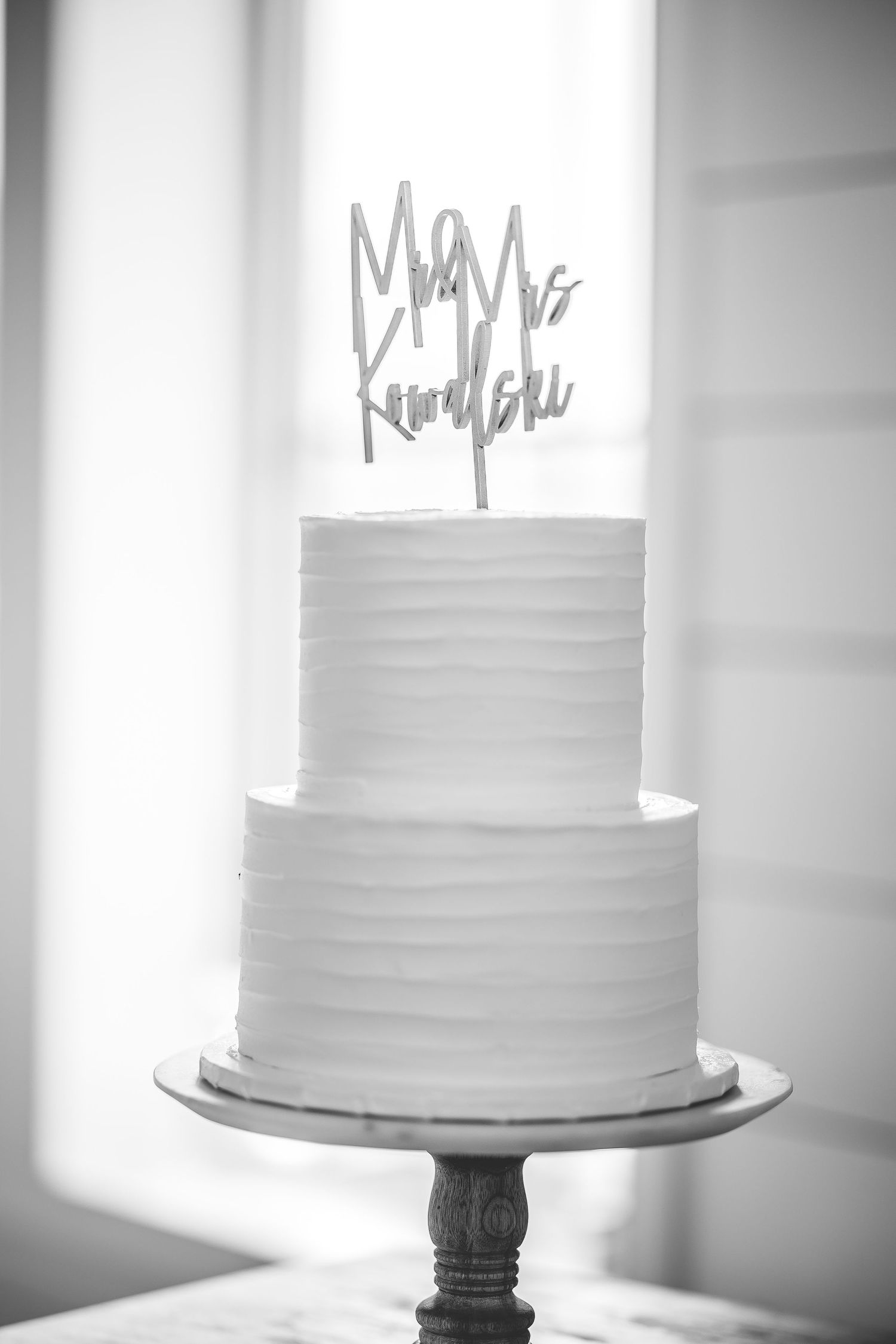 Elegant white wedding cakes displayed on dark stands against a bright background.