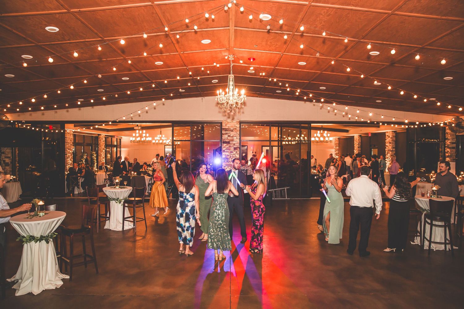 Large reception hall decorated with string lights and chandeliers for evening wedding celebration.