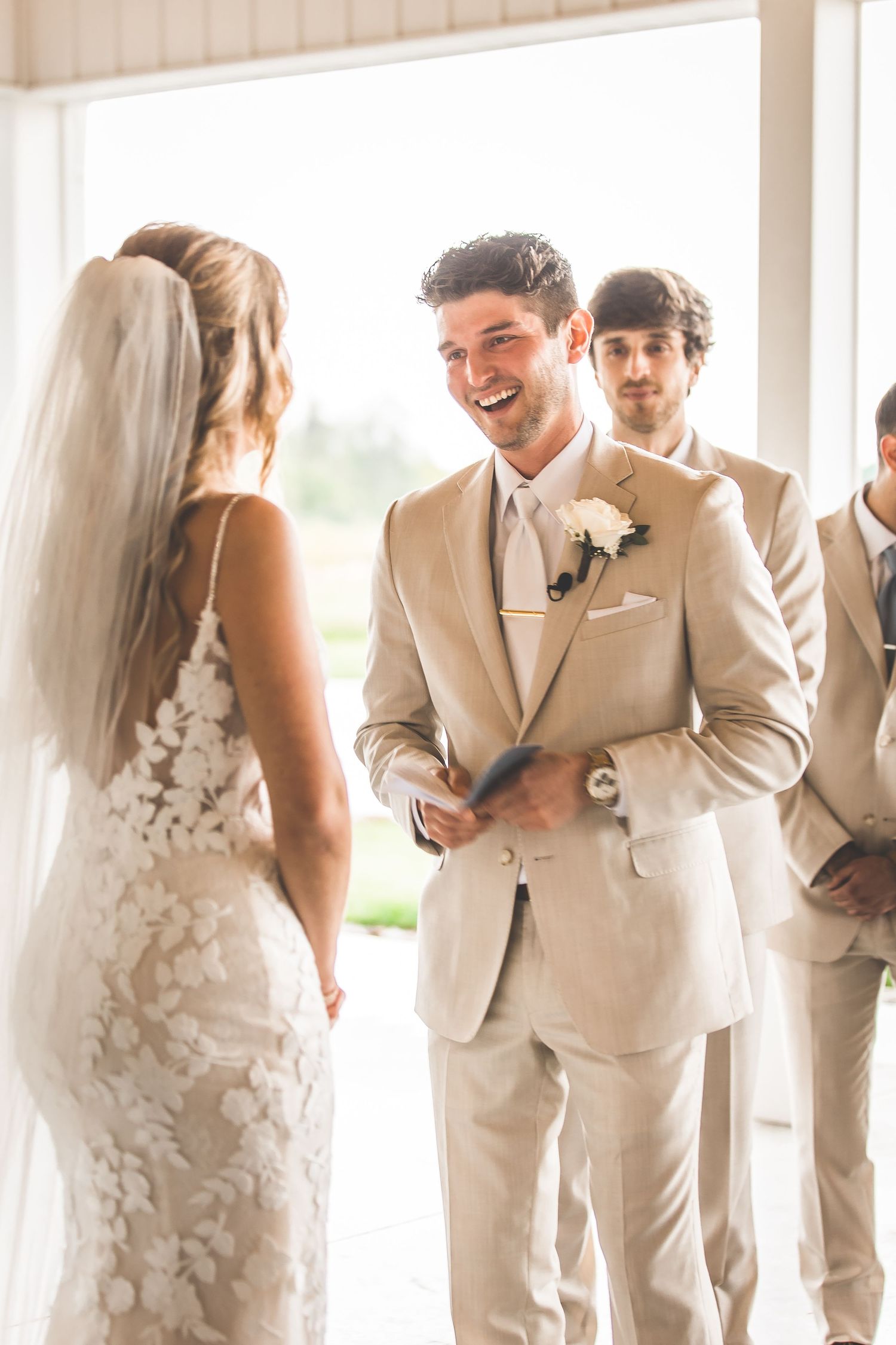 Wedding party members in beige suits and white dress gather for candid reactions.