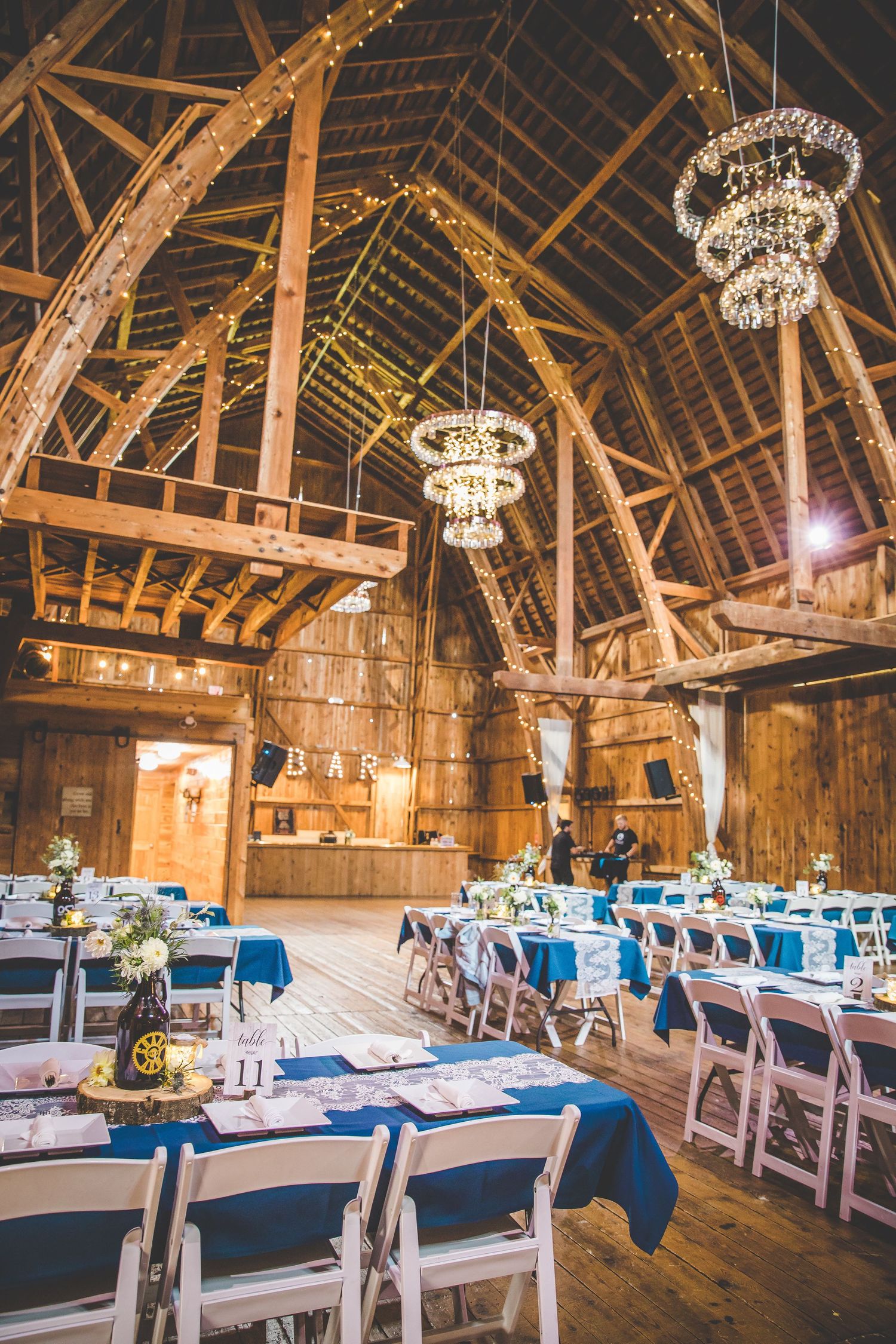 Rustic barn wedding reception venue decorated with elegant chandeliers and navy blue table settings.