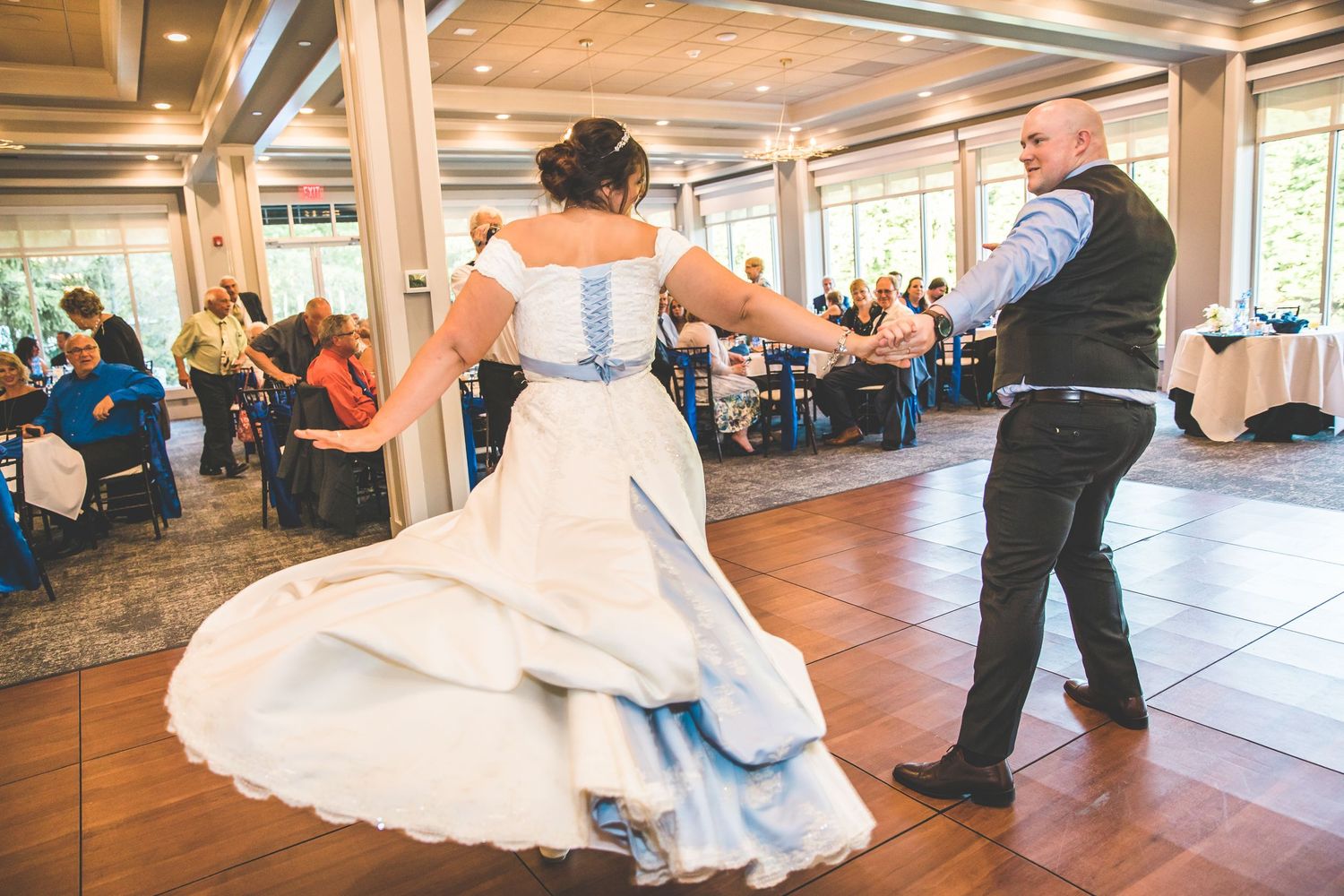 A couple dances during their wedding reception as the bride's white dress with blue accents twirls.