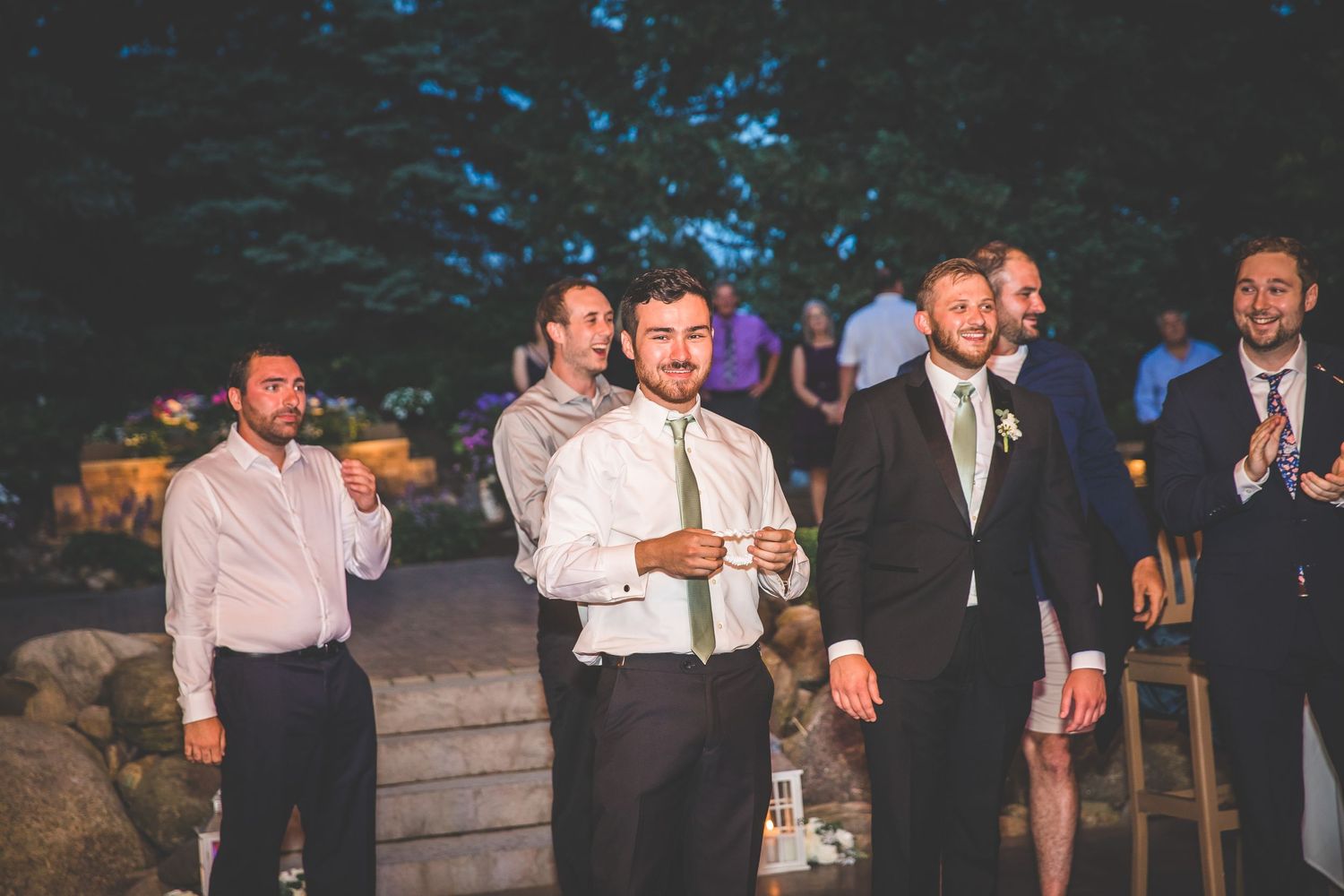 Groomsmen and guests gather outdoors during evening wedding festivities.