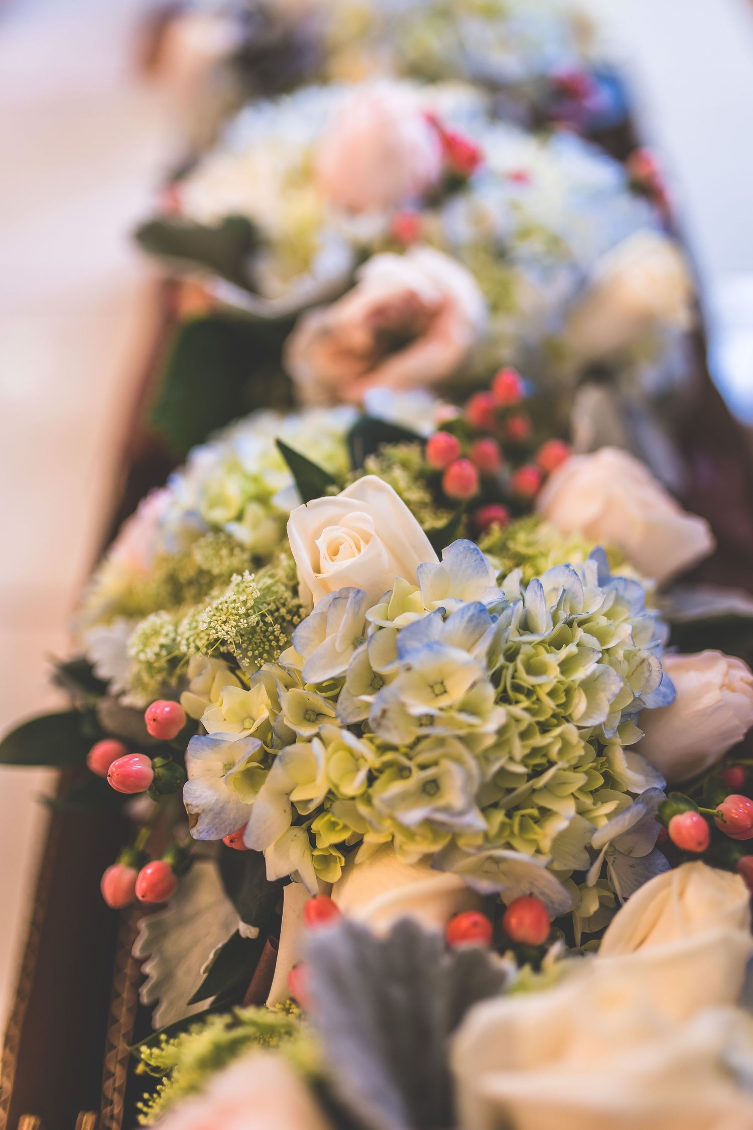 Elegant floral centerpiece with white hydrangeas and red berries in soft focus.