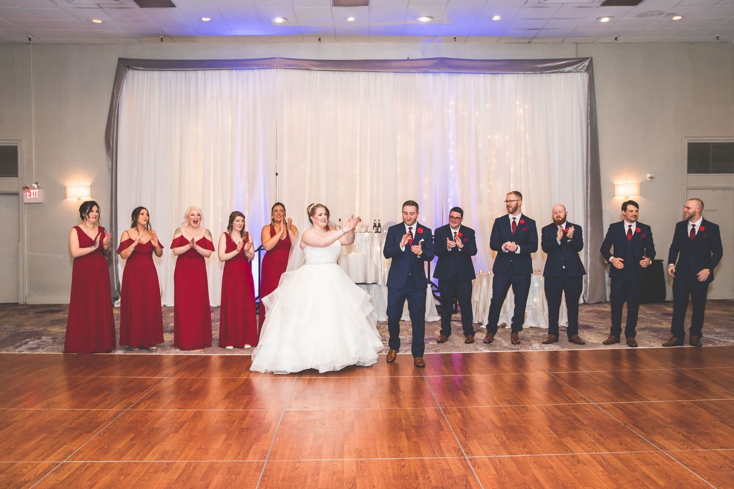 Wedding party lines up in burgundy dresses and navy suits on dance floor.