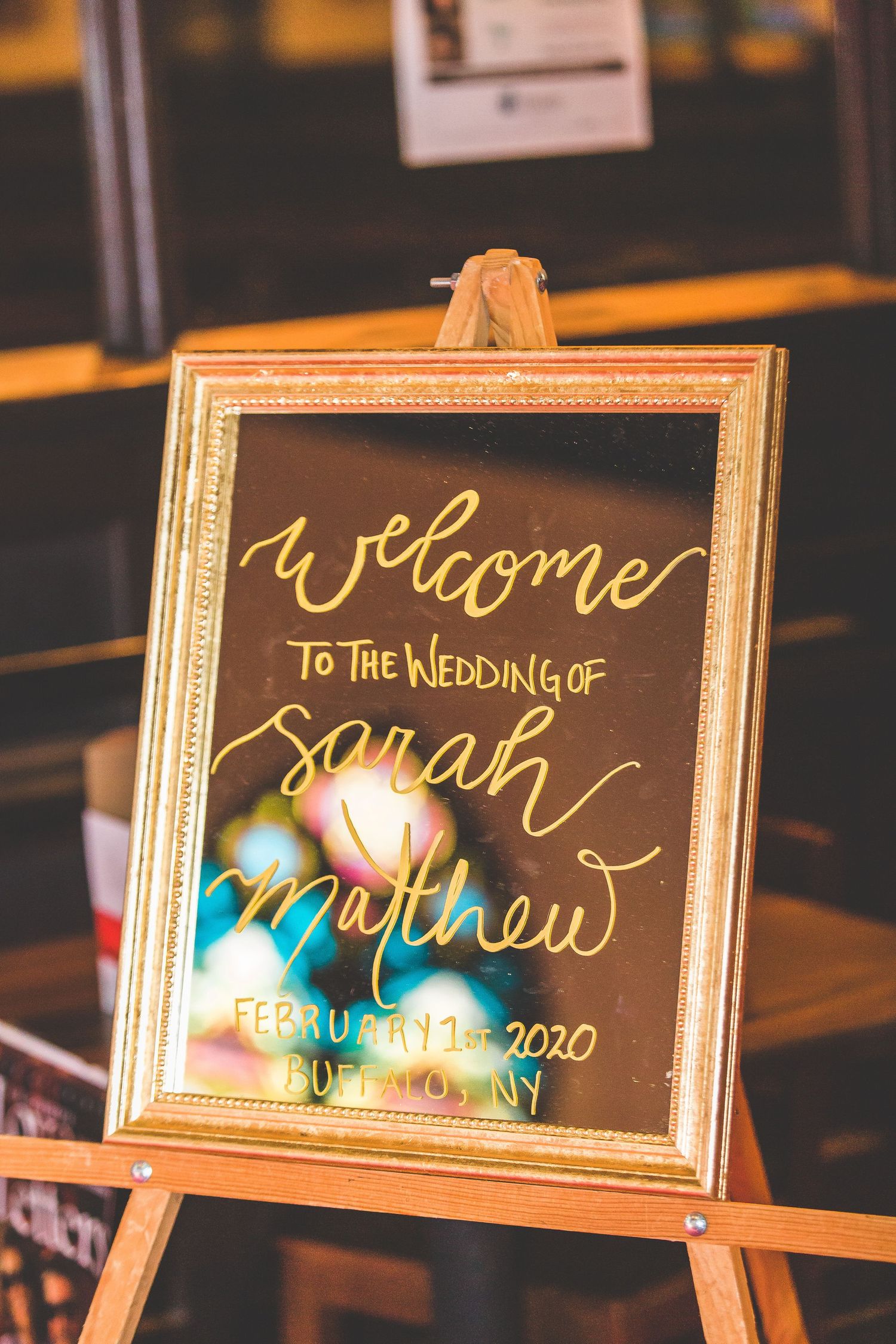 Elegant gold-framed welcome sign for Sarah and Matthew's wedding displayed on a wooden easel.